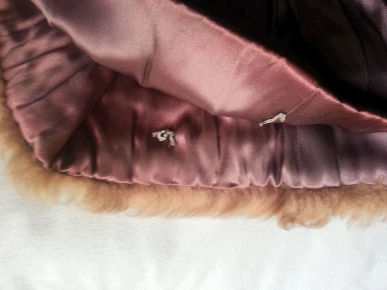 May include: A close-up of the inside of a brown fur coat. The lining is a soft, pink satin. The fur is a light brown color.