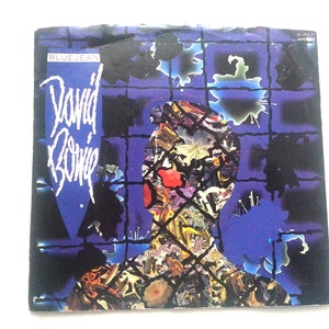 May include: A blue jean record single by David Bowie. The cover features a colorful abstract portrait of Bowie with a grid pattern in the background.
