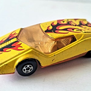 May include: Yellow toy car with black and red flames painted on the side. The car has a clear plastic windshield and orange accents.