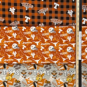 K&ouml;nnte beinhalten: Drei verschiedene Stoffe mit Texas-Motiv. Der obere Stoff ist orange und schwarz kariert mit "Texas"- und "T"-Logos. Der mittlere Stoff ist orange mit "Texas", Helmen und Longhorn-Logos. Der untere Stoff ist grau mit dem Texas-Maskottchen.
