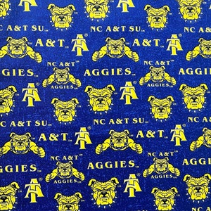 Może przedstawiać: Tkanina w kolorze niebieskim i żółtym z powtarzającym się tekstem "NC A&T SU" i "A&T Aggies". Wzór zawiera również żółtego buldoga maskotkę.