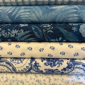 May include: A stack of fabric rolls in various blue and white patterns. The patterns include gingham, fern leaves, floral designs, and a toile-inspired print. The fabrics appear to be cotton or a similar material, suitable for quilting or home decor projects.