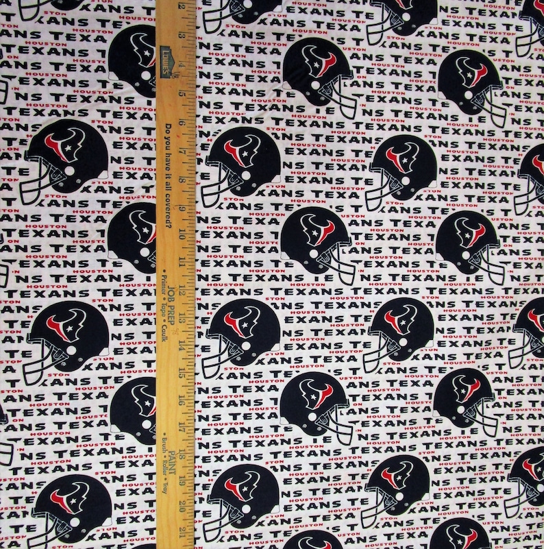 May include: Fabric featuring a repeating pattern of black Houston Texans football helmets with the team name in white and red on a white background. A wooden ruler is in the image.