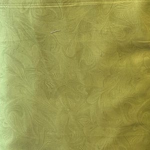May include: Close-up of a green fabric with a swirling, abstract pattern. The fabric has a subtle sheen and a smooth texture. The design features flowing, organic shapes in varying shades of green.