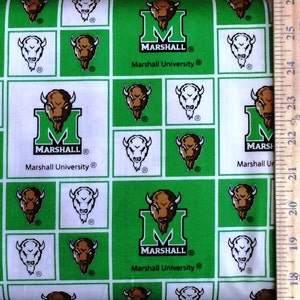 May include: Green and white fabric with a repeating pattern of a green "M" for Marshall University, a bison head, and a white bison head. The fabric is measured with a ruler.