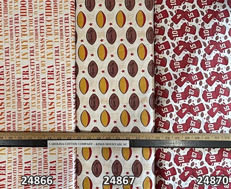 K&ouml;nnte beinhalten: Stoffmuster mit Football-Motiven. Designs umfassen Footballs, Trikots und Text, der "Kansas City Era" und "In My Touchdown Era" lautet. Der Stoff stammt von Carolina Cotton Company.