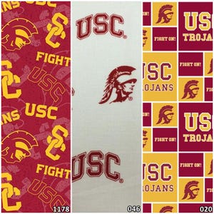 May include: Three fabric swatches with USC Trojans designs. One features a repeating pattern of the USC logo and Trojan head in cardinal red and gold. Another has the USC logo and Trojan head on a white background. The third has a repeating pattern of the USC logo, Trojan head, and text.