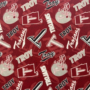 May include: A maroon fabric with a repeating pattern of the word "TROY", football helmets, and the word "Trojans". The letter "T" is also featured in the design. The design is in white, black, and gray.