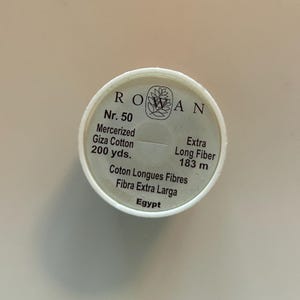 May include: A white spool of Rowan Nr. 50 mercerized Giza cotton thread. The label includes the text "200 yds." and "Extra Long Fiber 183 m." The spool also has the text "Coton Longues Fibres", "Fibra Extra Larga", and "Egypt".