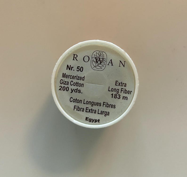 May include: A white spool of Rowan Nr. 50 mercerized Giza cotton thread. The label includes the text "200 yds." and "Extra Long Fiber 183 m." The spool also has the text "Coton Longues Fibres", "Fibra Extra Larga", and "Egypt".