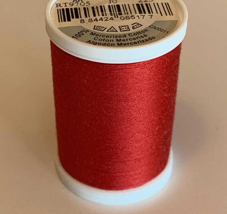 May include: A spool of bright red mercerized cotton thread. The spool has a white base and top with printed text, including "100% Mercerized Cotton". The thread is tightly wound, showing a smooth, even texture. Ideal for sewing and crafting projects.