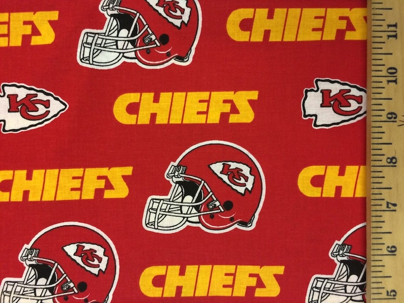 K&ouml;nnte beinhalten: Roter Stoff mit einem sich wiederholenden Muster aus Kansas City Chiefs Helmen, Logos und dem Wort "CHIEFS" in Gelb. Ein Lineal zeigt die Ma&szlig;e in Zentimetern.