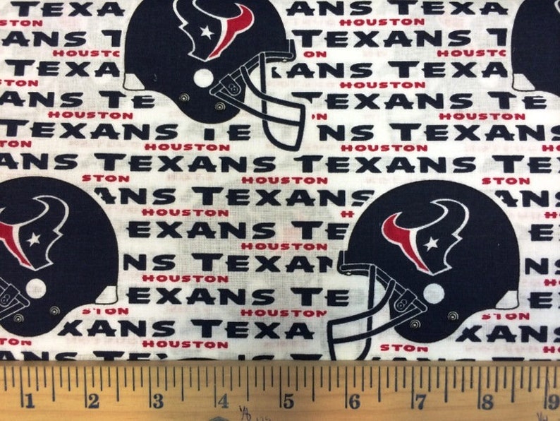 May include: White fabric with a repeating pattern of navy blue Houston Texans football helmets and the words "TEXANS" and "HOUSTON" in black and red. The fabric is likely cotton or a similar material.