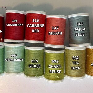 May include: A collection of colorful thread spools in various shades, including red, green, blue, and gold. Each spool is labeled with a color name and number, such as "Cinnamon" and "Cranberry". The spools are arranged in neat rows.