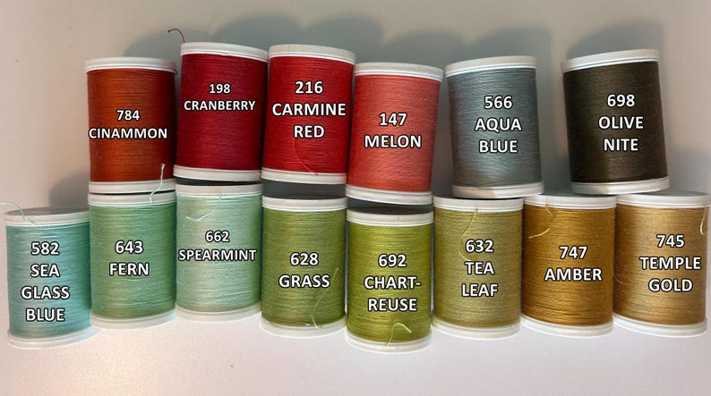 May include: A collection of colorful thread spools in various shades, including red, green, blue, and gold. Each spool is labeled with a color name and number, such as "Cinnamon" and "Cranberry". The spools are arranged in neat rows.