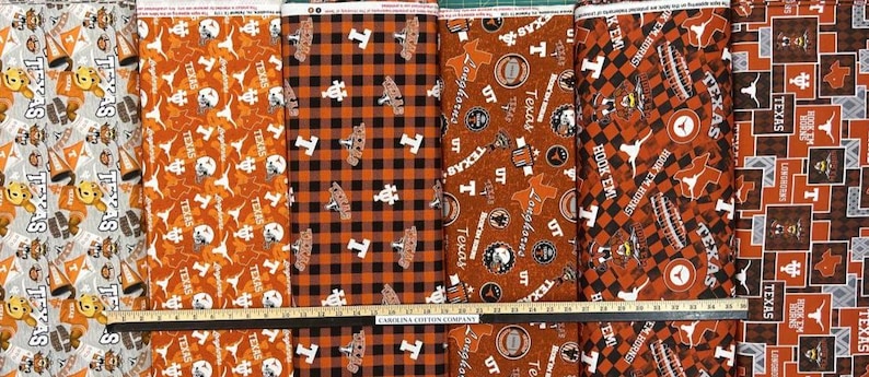 K&ouml;nnte beinhalten: Eine Auswahl an Stoffmustern mit dem Text "TEXAS" und Longhorn-Motiven in Orange, Wei&szlig; und Schwarz. Designs umfassen sich wiederholende Muster, Karomuster und Logoanordnungen. Ein Lineal liegt unten.