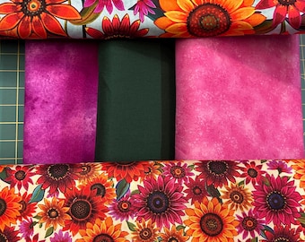 May include: A collection of folded fabric bolts featuring two distinct floral patterns with sunflowers in shades of red, orange, and pink, alongside three solid-colored fabric bolts in deep purple, dark forest green, and bright magenta.