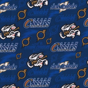 Peut inclure: Tissu bleu avec un motif répété d'une mascotte de dessin animé blanche avec une batte de baseball, les mots "Storm Chasers" en bleu et or, et un anneau doré.
