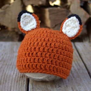 May include: A crocheted fox hat with orange, white, and black yarn. The hat has two large, floppy ears.