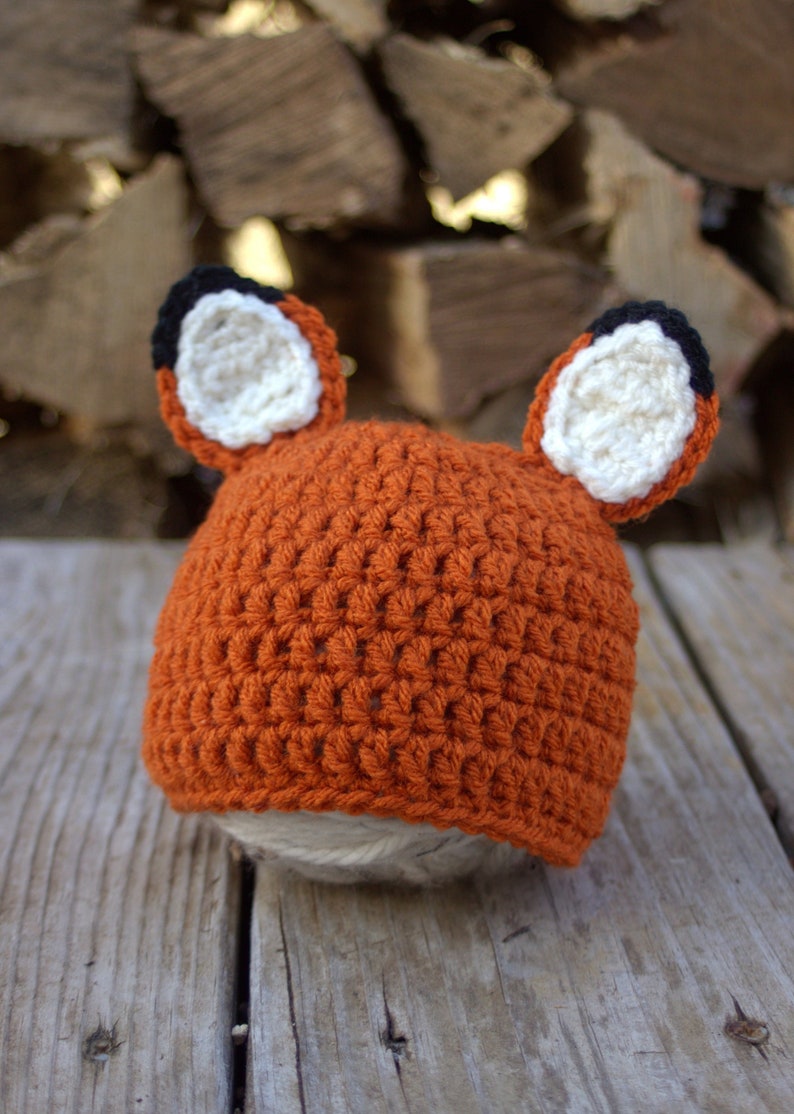 May include: A crocheted fox hat with orange, white, and black yarn. The hat has two large, floppy ears.