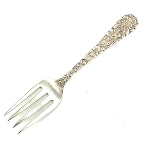 Pode incluir: Um garfo de prata com um design floral no cabo. O garfo tem três dentes e está em bom estado.