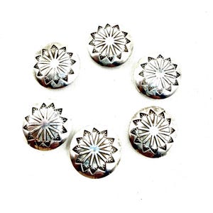 Könnte beinhalten: Ein Set aus fünf kreisförmigen, silberfarbenen Metall-Conchos, die jeweils ein gestanztes Sonnen- oder Sternenmuster aufweisen, das von der Mitte ausstrahlt. Die Designs bestehen aus abwechselnd langen und kurzen Linien.