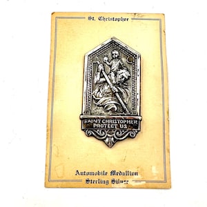 Könnte beinhalten: Ein silbernes Saint-Christopher-Medaillon auf einer Karte mit der Aufschrift "Saint Christopher Protect Us" und "Automobile Medallion Sterling Silver".