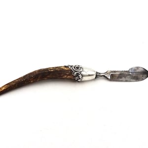 Könnte beinhalten: Ein vintage Messer mit einem gewellten Messer, einem Griff aus Silber und Hirschhorn. Der Griff ist mit einem floralen Muster verziert.