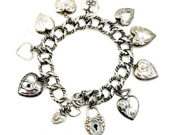 May include: A silver charm bracelet featuring a thick, textured chain link design. The bracelet is adorned with multiple heart-shaped charms, including several engraved with floral patterns, one with a padlock design, and one with the letters AEB.