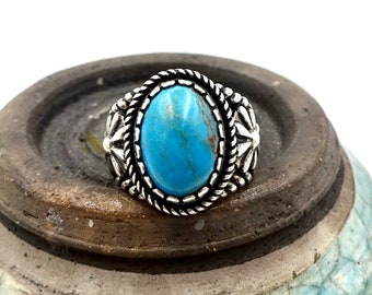 Könnte beinhalten: Ein silberner Ring mit einem blauen Türkis-Stein, der in einer detaillierten ovalen Fassung sitzt. Der Ring hat ein seilartiges Design um den Stein und florale Akzente an den Seiten.