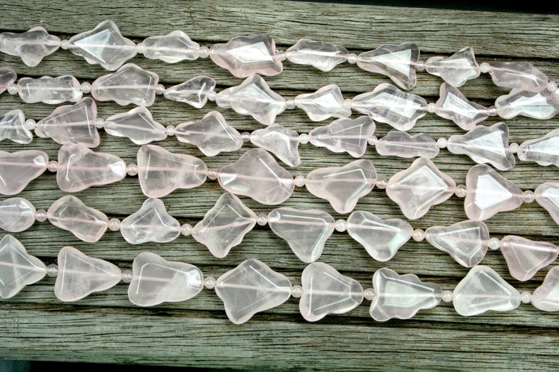 May include: A strand of pink rose quartz beads, each bead is faceted and shaped like a teardrop. The beads are strung on a clear elastic cord and are arranged in a staggered pattern.