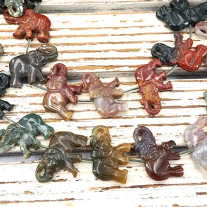May include: A strand of gemstone elephant beads, each carved from a different type of agate. The beads are strung on a wire and are a variety of colors, including green, brown, red, and white.