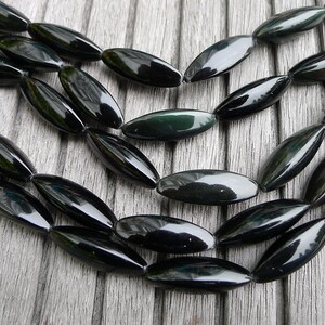 May include: A strand of black and green gemstone beads, each bead is oval shaped and polished.