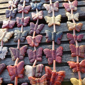 May include: A strand of gemstone butterfly beads in various colors, including red, black, white, and brown. The beads are strung on a clear cord and are arranged in a repeating pattern.
