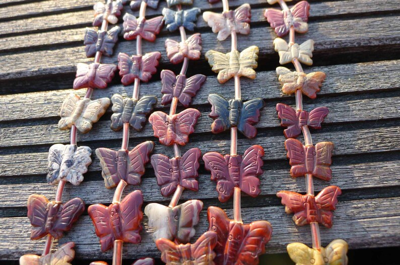 May include: A strand of gemstone butterfly beads in various colors, including red, black, white, and brown. The beads are strung on a clear cord and are arranged in a repeating pattern.