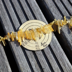 May include: A string of yellow and clear crystal beads laid out on a wooden surface. The beads are arranged in a line and are all different shapes and sizes. A round target with the words "Sparkle Little" and numbers 30, 40, and 50 is visible in the background.
