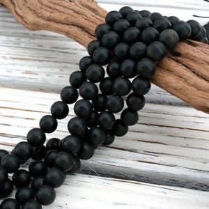 May include: A strand of black onyx beads, round and smooth, displayed on a piece of driftwood. The beads are arranged in a cascading pattern, highlighting their polished surface.