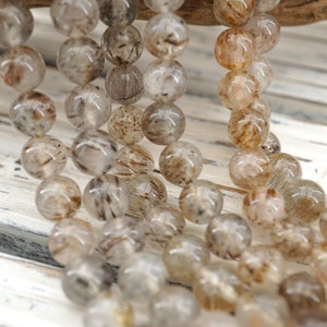 May include: A strand of round, translucent beads with brown and black inclusions. The beads are strung together on a clear thread.