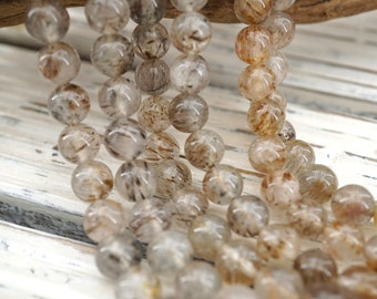 May include: A strand of round, translucent beads with brown and black inclusions. The beads are strung together on a clear thread.