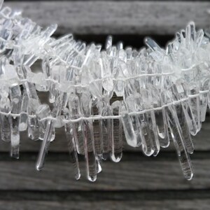 May include: A strand of clear quartz crystal points, strung together with white thread. The points are various lengths and are arranged in a cascading pattern.