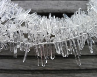 May include: A strand of clear quartz crystal points, strung together with white thread. The points are various lengths and are arranged in a cascading pattern.