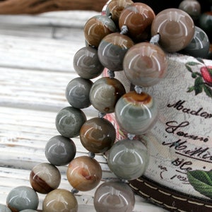 May include: A strand of grey, brown, and white gemstone beads in a floral patterned box. The box has the text "Mademoiselle Souvenir Sohn" written on it.