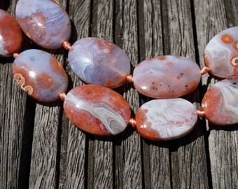 May include: A strand of oval-shaped agate beads with a mix of white, orange, and brown colors. The beads are strung on a cord with a copper-colored thread.