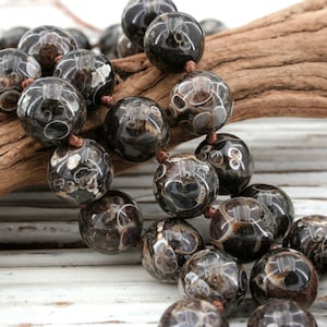 May include: A strand of black and white agate beads with a swirling pattern. The beads are round and have a smooth, polished finish. The beads are strung on a brown cord.