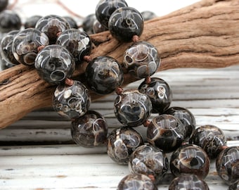 May include: A strand of black and white agate beads with a swirling pattern. The beads are round and have a smooth, polished finish. The beads are strung on a brown cord.