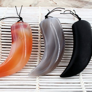 May include: Three polished stone pendants in a horn shape, each with a black cord for hanging. The pendants are in shades of orange, gray, and black, displayed on a white bamboo mat.