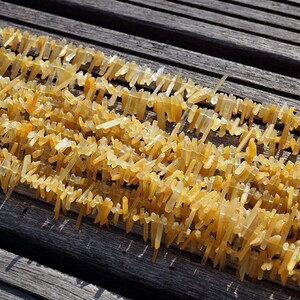 May include: A strand of yellow crystal beads, each bead is a long, thin, pointed crystal. The beads are arranged in rows on a wooden surface.