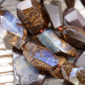 May include: A strand of brown and blue opal gemstone beads. The beads are faceted and have a rough, natural look.