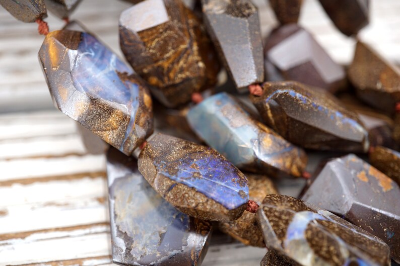 May include: A strand of brown and blue opal gemstone beads. The beads are faceted and have a rough, natural look.