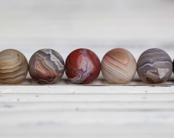 May include: A row of six agate beads, each with a unique pattern of brown, white, and red stripes. The beads are arranged in a line on a white surface.